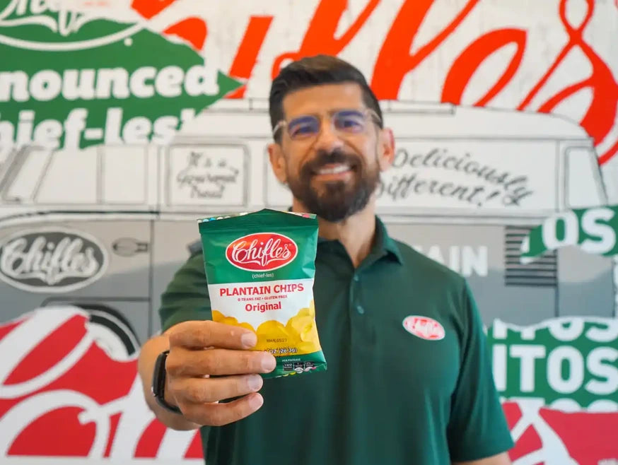 Tony Rivas holding a bag of Chifles Original plantain chips in front of a Chifles mural